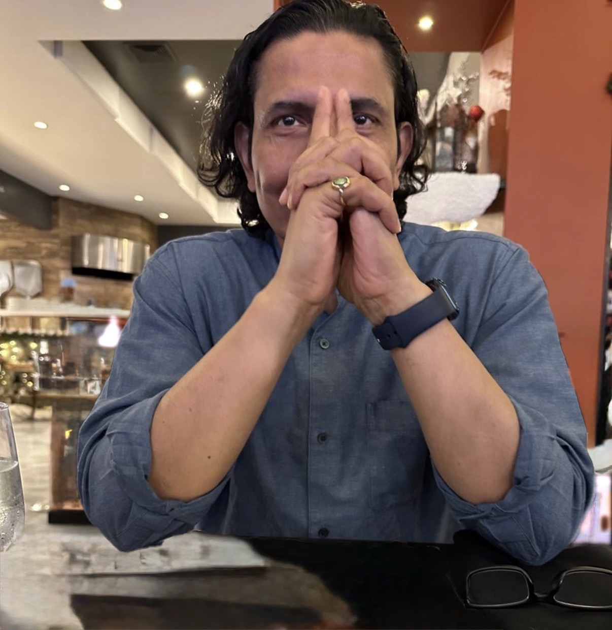 Ron Mukherjee seated at a table, hands resting together, listening